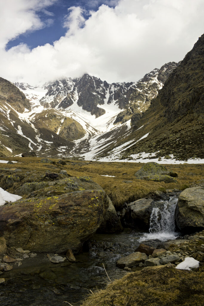 Dramatic mountain landscape with snowy peaks rugged rocks and clear alpine stream wallpaper background