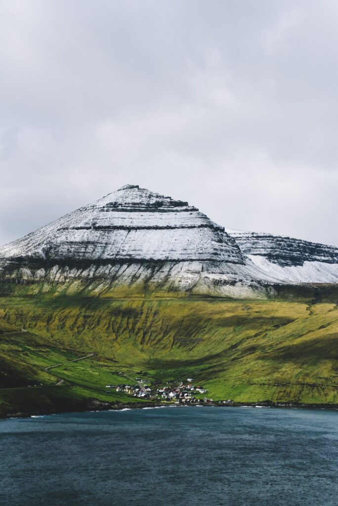 Snow-capped mountain over green valley with buildings and deep blue shore natural landscape wallpaper