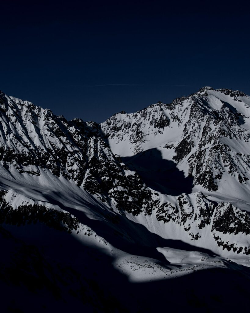 Snowy mountain peak at night with dark sky creating a dramatic and serene wallpaper background