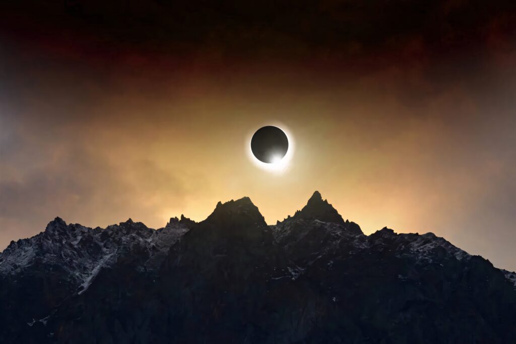 Dramatic solar eclipse over rugged cloudy mountaintop casting golden glow on dark peaks Wallpaper