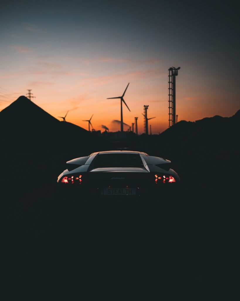 Sleek Sports Car Silhouette against Dusky Sky & Wind Turbines Wallpaper