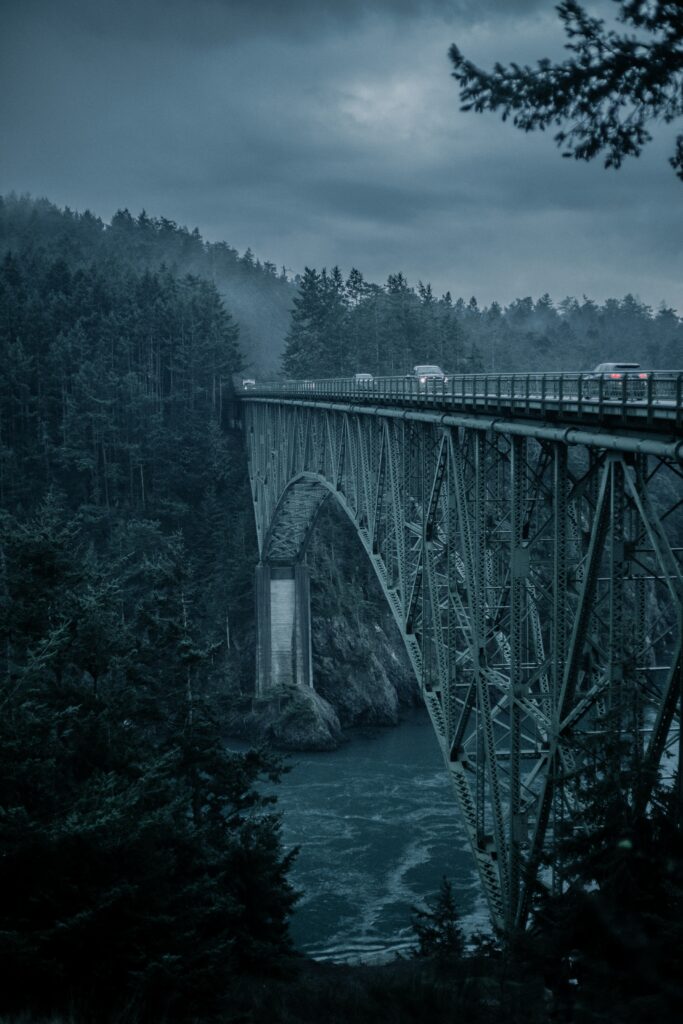 Dramatic steel bridge over river with evergreen forests misty mountains evening wallpaper background