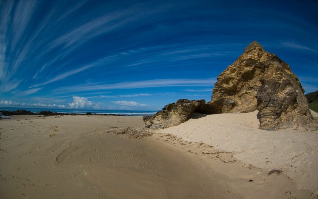 Dramatic stone formations on sandy beach with swirling clouds over deep blue sky wallpaper background