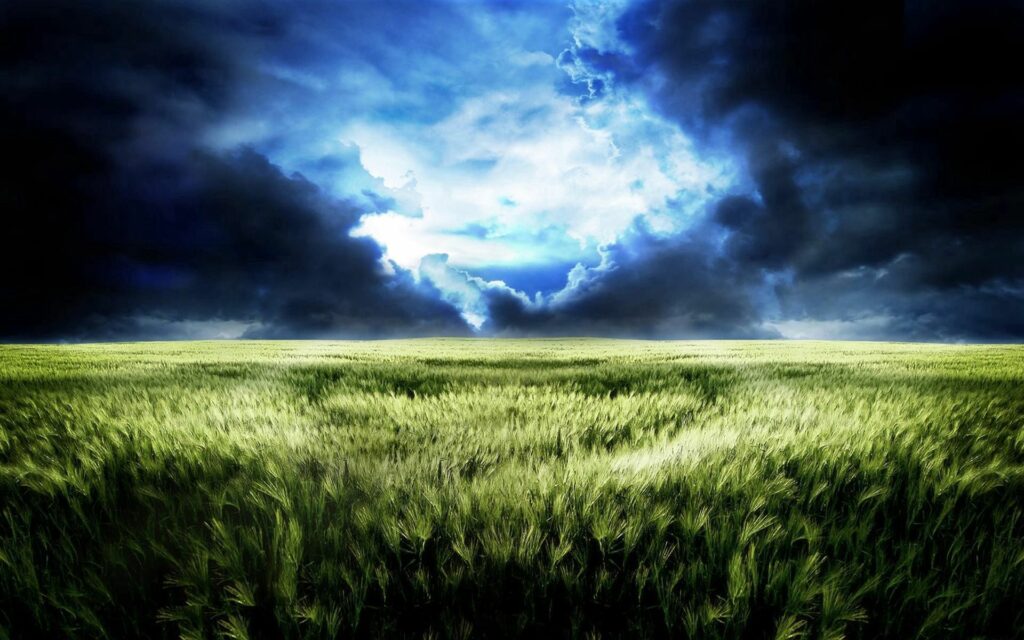 Vast green field under dark blue storm clouds with bright light piercing gloomy sky wallpaper background