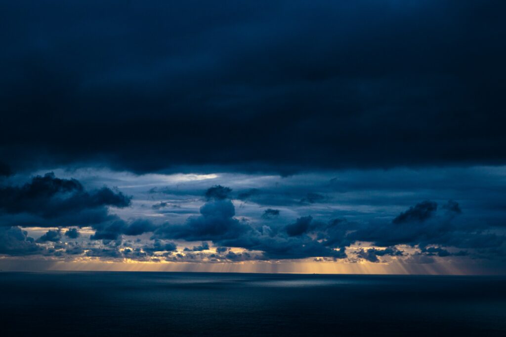 Dramatic stormy seascape with golden sunlight piercing dark clouds over calm blue sea wallpaper
