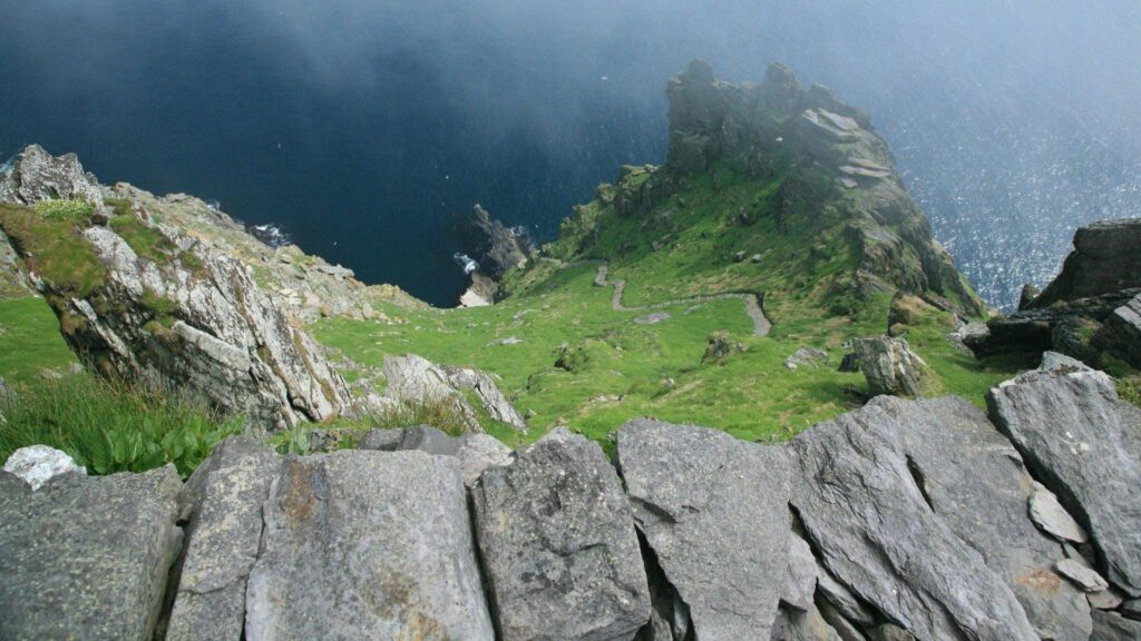 Summer landscape with lush grass rocky cliffs and deep blue water panoramic nature wallpaper