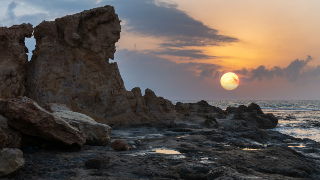 Dramatic summer sunset over sea with rugged rocks glowing orange and gold tranquil wallpaper