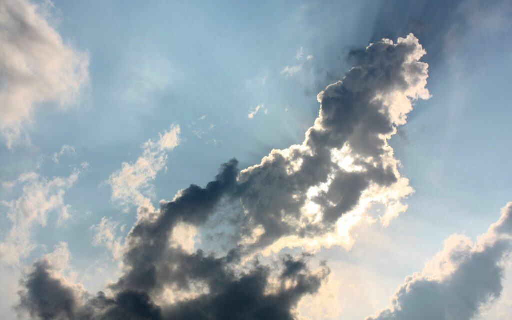 Dramatic sky wallpaper with sunlit billowing clouds bright rays and deep shadows on blue background