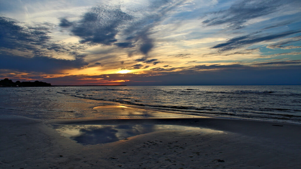 Sunset beach wallpaper with dark clouds calm sea gentle waves and golden blue tidal pool reflections