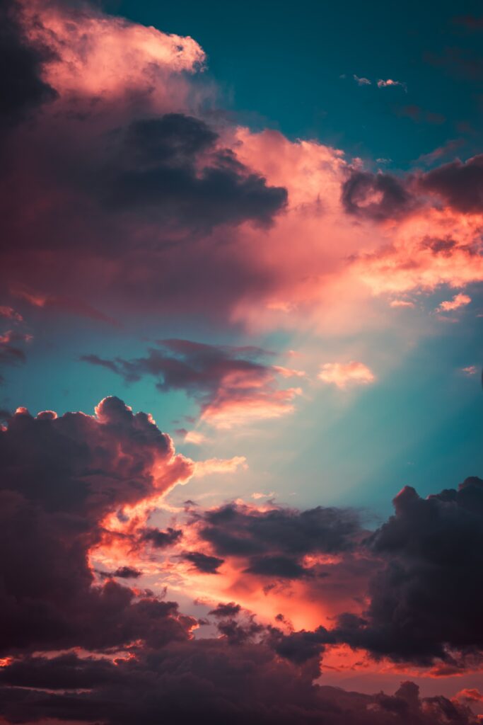 Dramatic sunset sky with porous clouds in blue pink and orange rays breaking through clouds Wallpaper