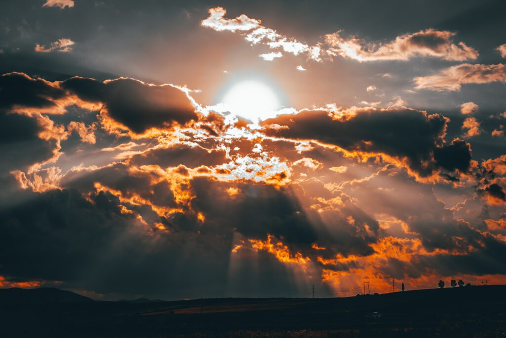 Dramatic sunset clouds with vibrant orange gold rays piercing high contrast atmospheric sky Wallpaper