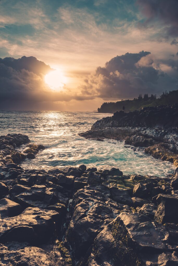 Dramatic coastal sunset with rugged rocks waves crashing and glowing sun breaking through clouds Wallpaper