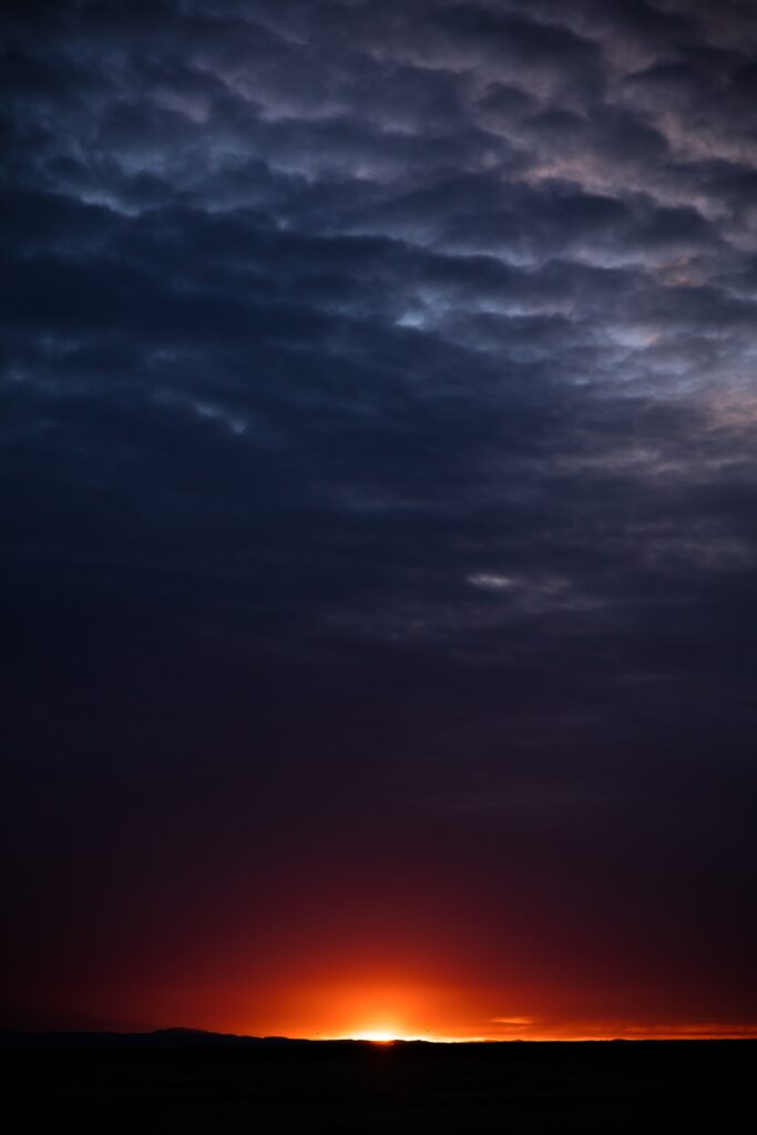 Dramatic sunset horizon with deep orange light and textured violet clouds night sky wallpaper