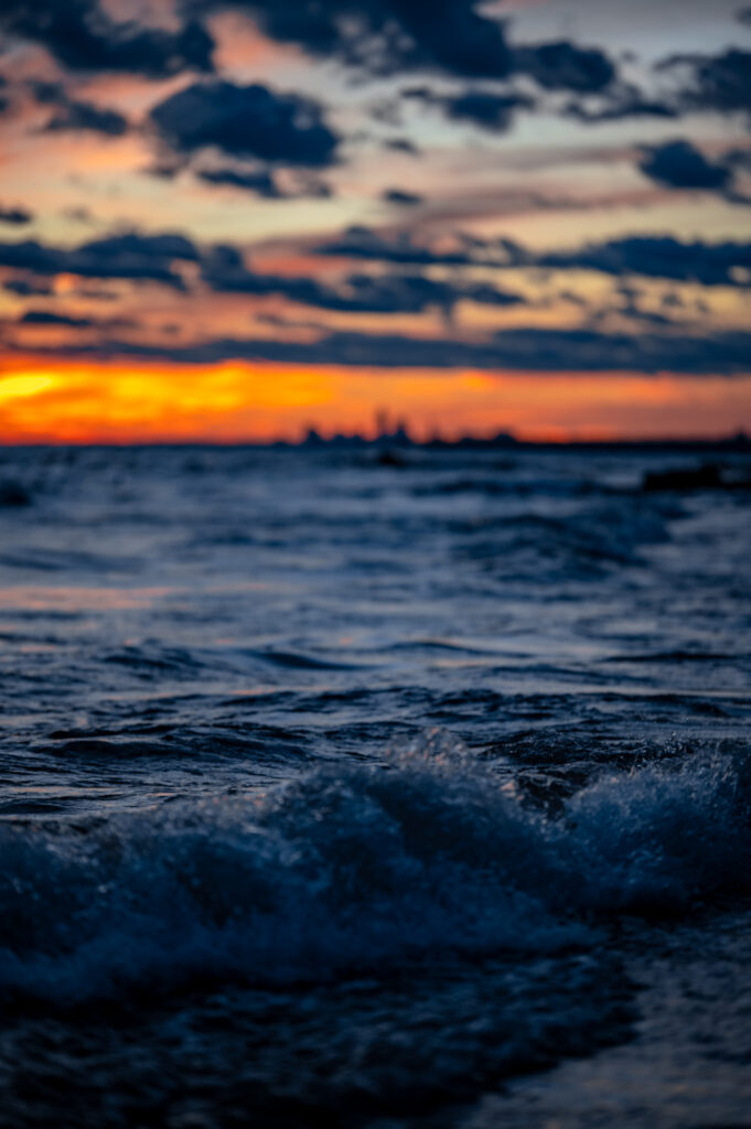 Dynamic ocean waves with sunset sky blending deep blues and fiery orange horizon wallpaper background