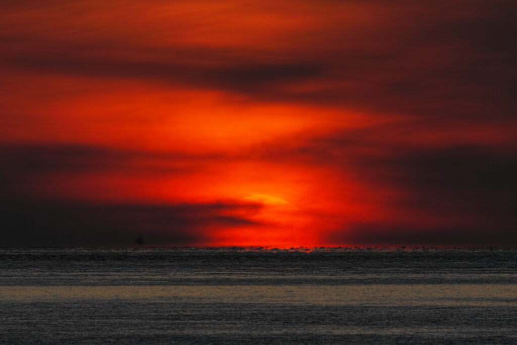 Dramatic sunset over sea with orange red sky dark clouds and rippling water wallpaper background