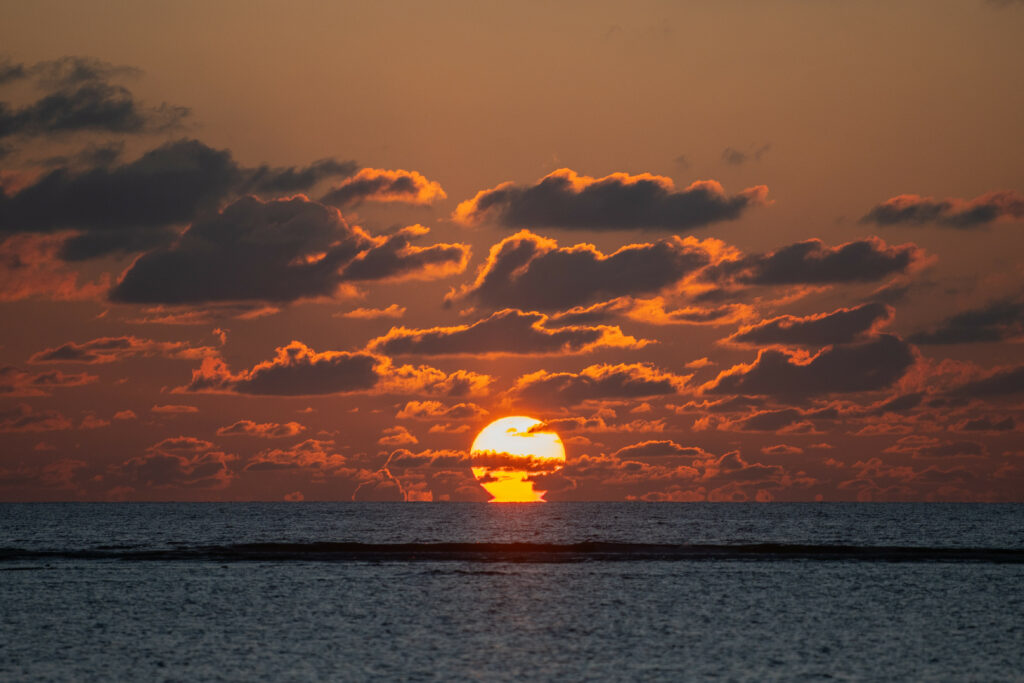 Dramatic sunset over calm sea with vibrant orange sky and dark clouds on horizon at dusk wallpaper