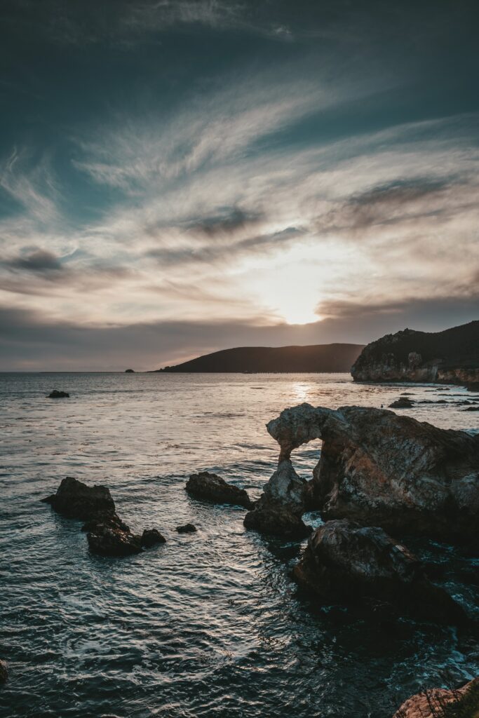 Dramatic sunset over sea with rocky foreground and colorful clouds peaceful coastal wallpaper