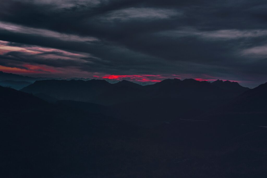 Dramatic sunset over rolling hills and jagged mountains with fiery red horizon and dark sky Wallpaper