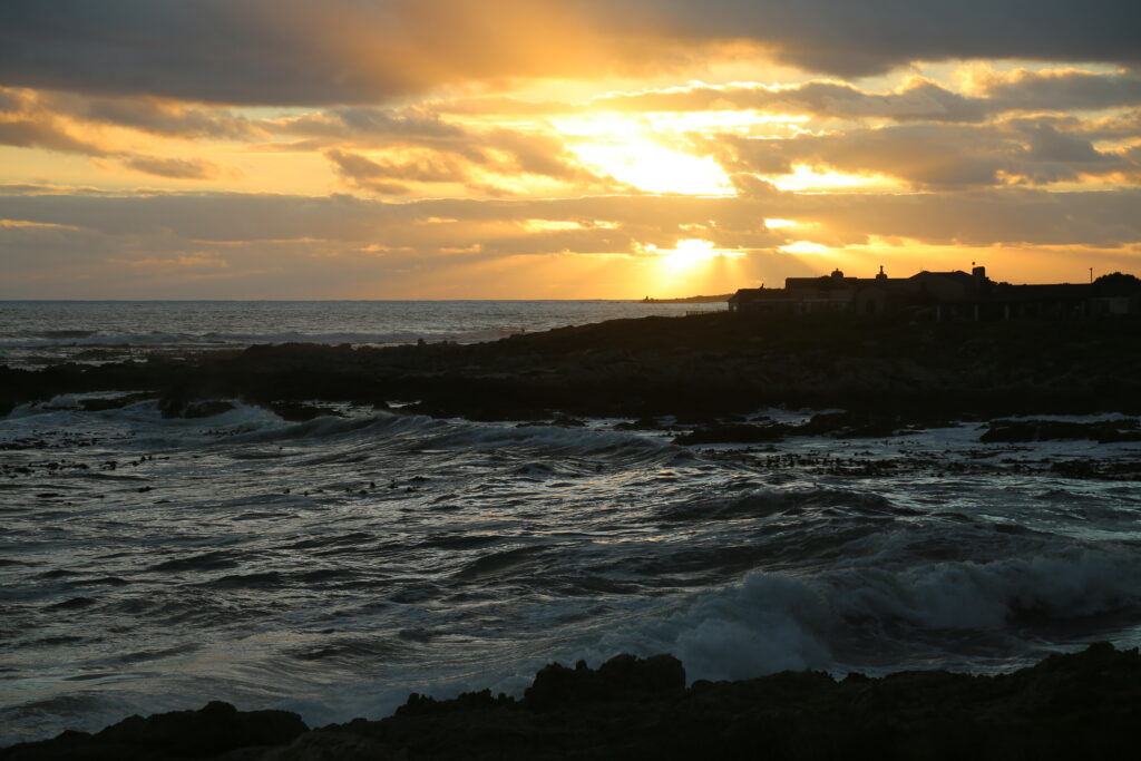 Dramatic sunset over rugged island coastline with dark waves and moody sky at dusk wallpaper