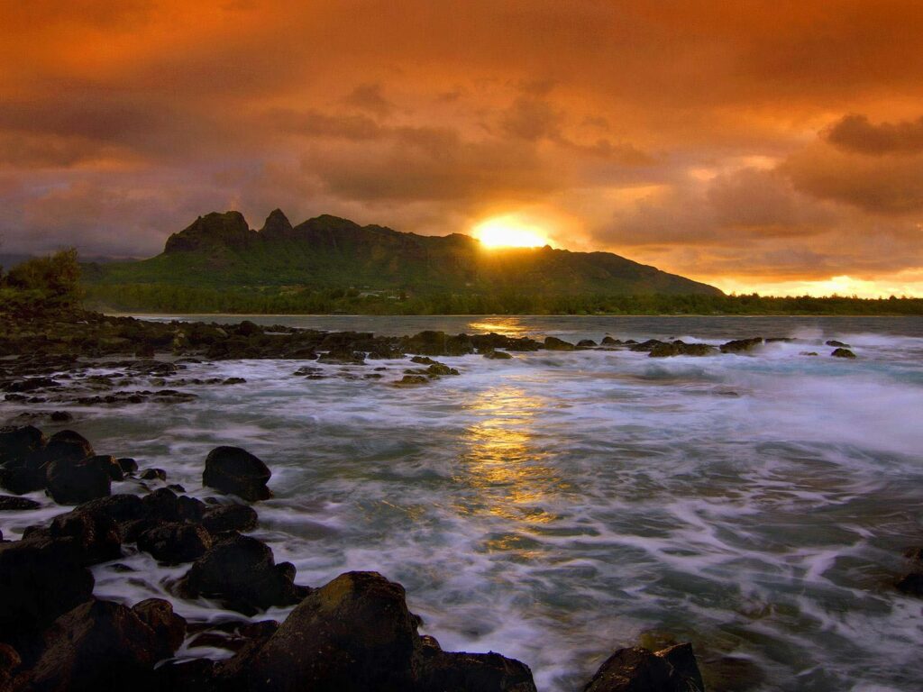 Dramatic sunset over rugged island with crashing sea waves rocky coast vibrant orange clouds Wallpaper