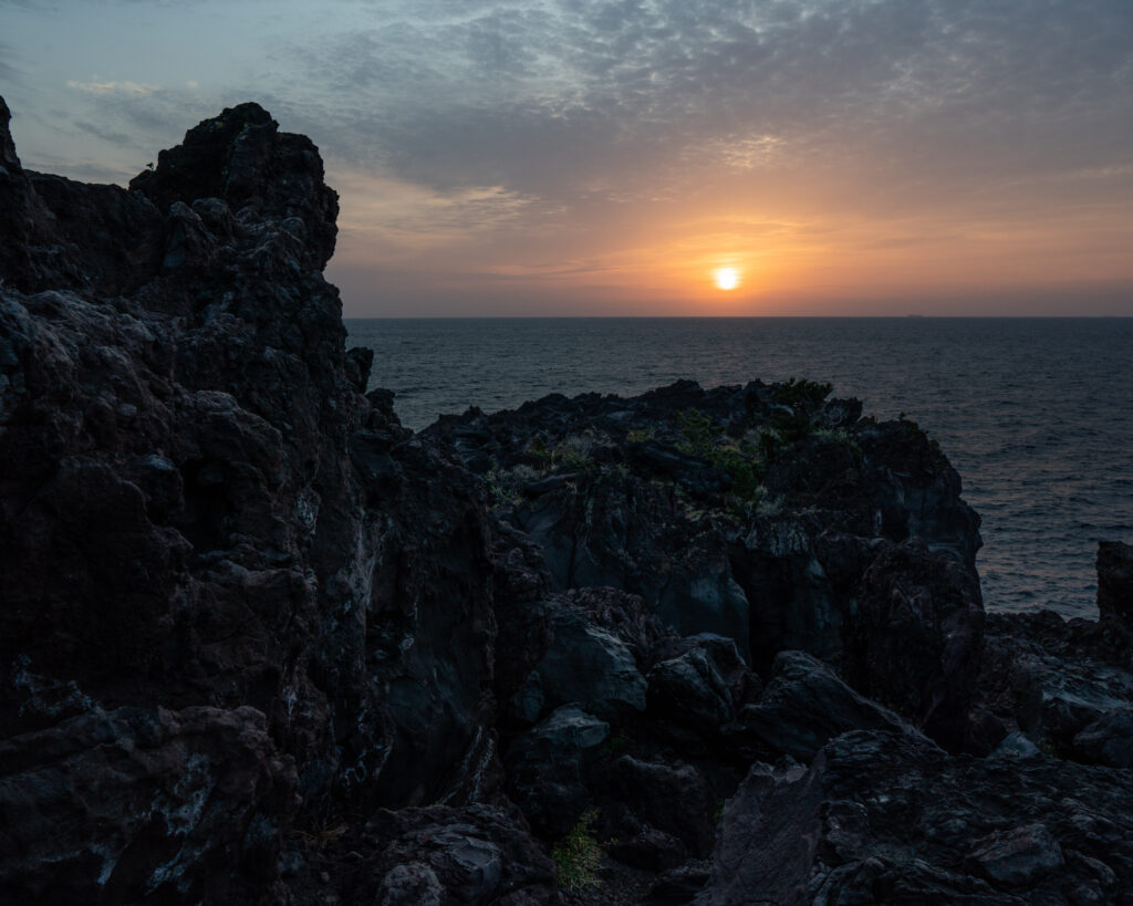 Dramatic sunset over rugged ocean rocks warm orange sunlight reflecting on water and clouds Wallpaper
