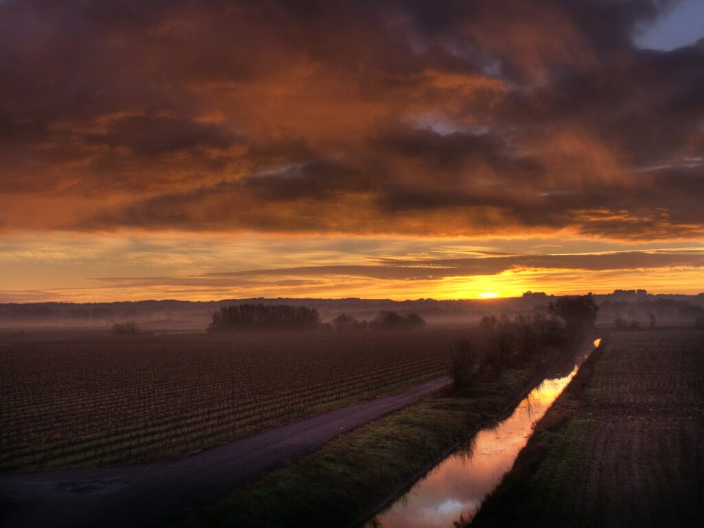 Dramatic sunset sky over vast rural field with winding road and reflective waterway horizon view Wallpaper