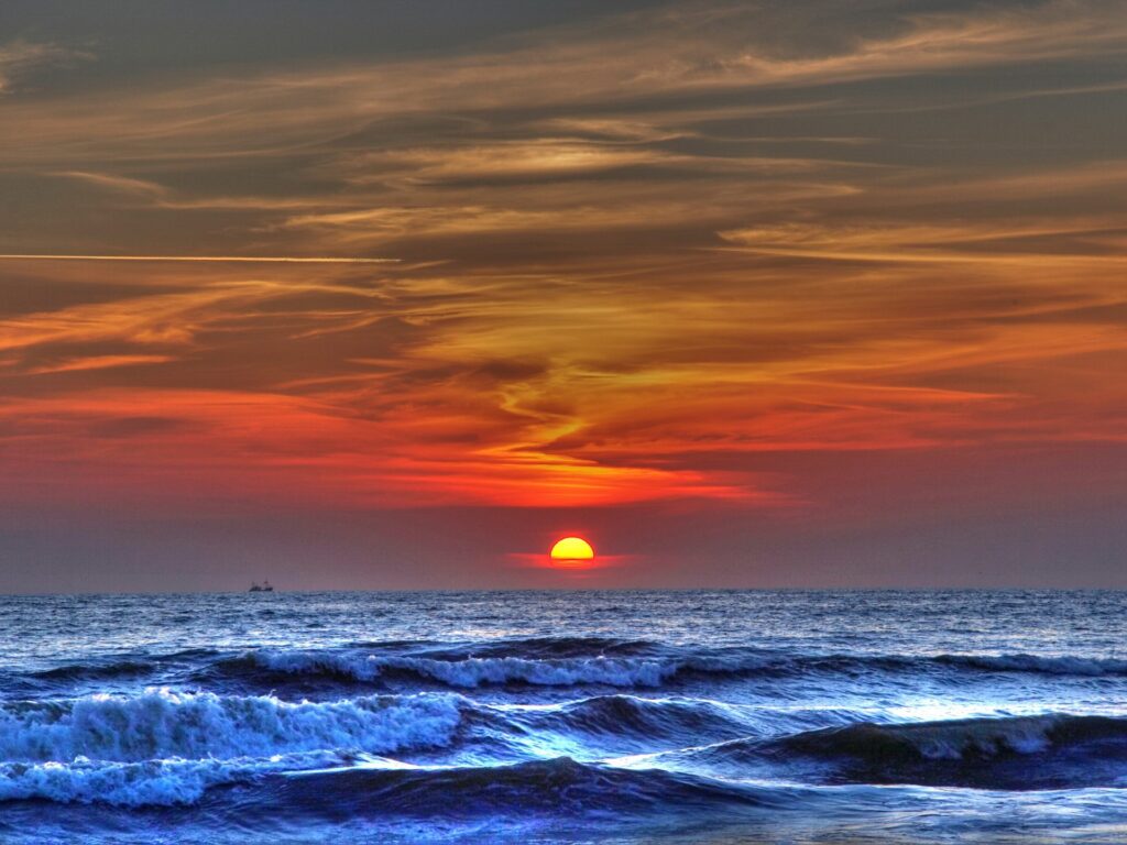 Dramatic sunset sky with orange and blue hues over restless waves in stormy sea wallpaper background