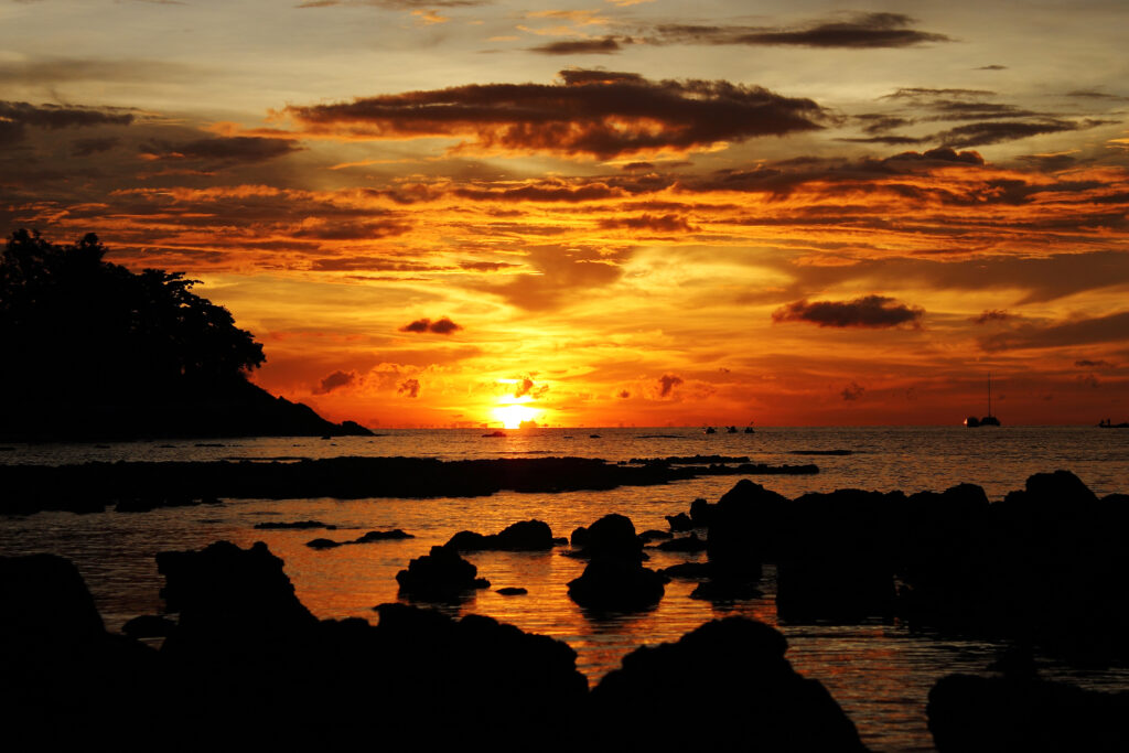 Dramatic sunset over tranquil sea with orange golden hues and dark stones silhouette wallpaper