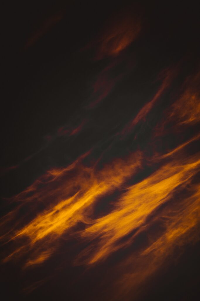 Porous clouds lit by vibrant orange and red sunset against dark moody sky wallpaper background