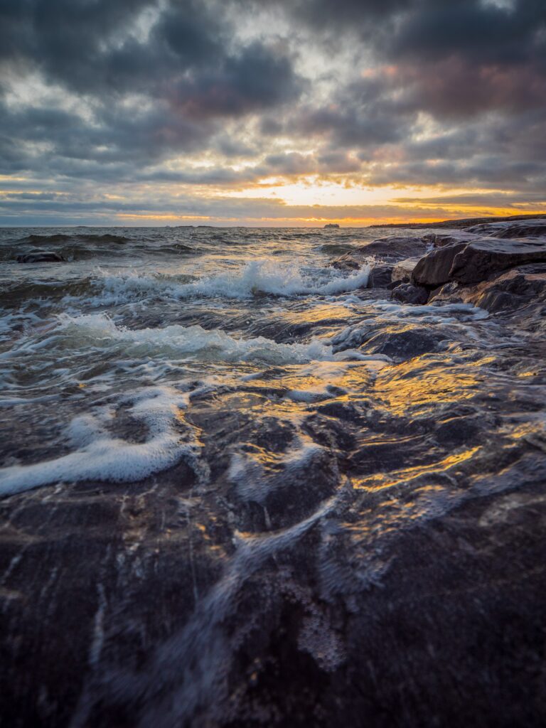 Dramatic seascape wallpaper with foaming waves crashing dark rocks under vivid sunset sky