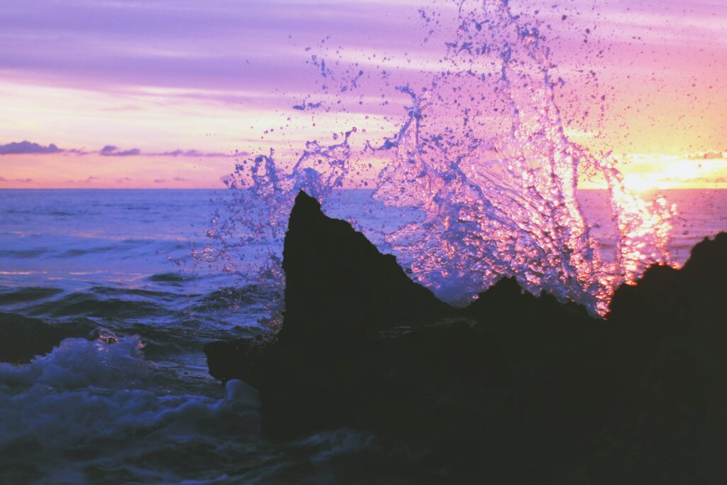 Dramatic seascape with jagged rocks crashing waves vibrant pink purple sunset over calm sea wallpaper