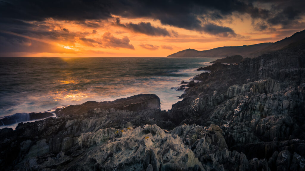 Dramatic sunset seascape with rugged rocks vibrant orange sky and tranquil coastal waves wallpaper