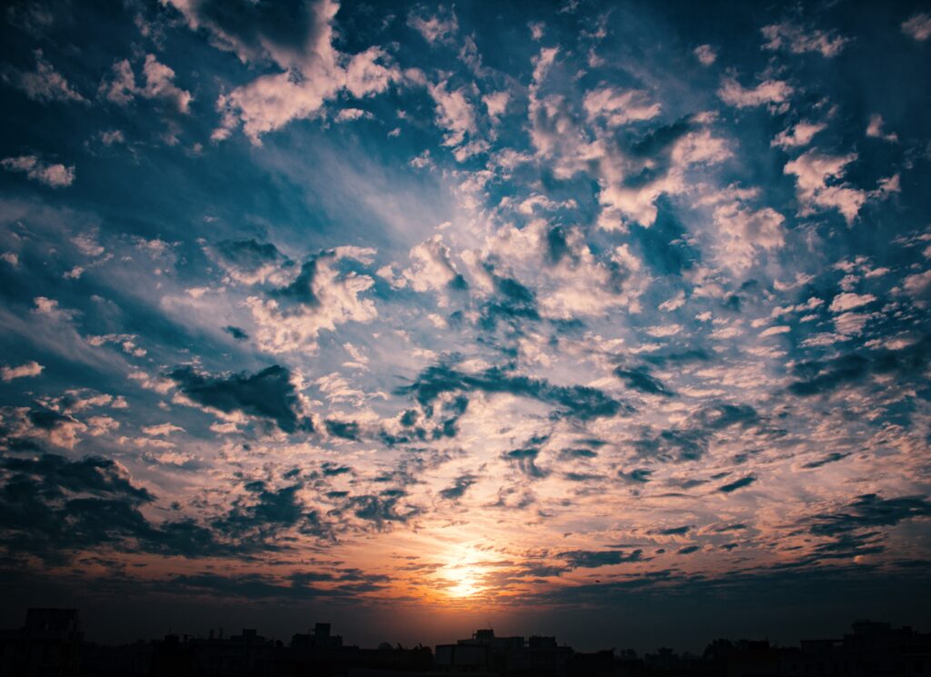 Dramatic sunset sky with scattered clouds in deep blue orange and golden tones wallpaper background