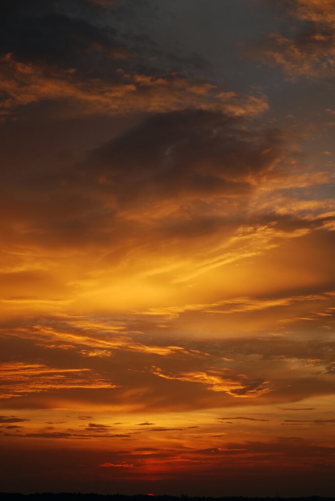 Dramatic sunset sky with dark clouds and vibrant orange golden hues over evening horizon wallpaper