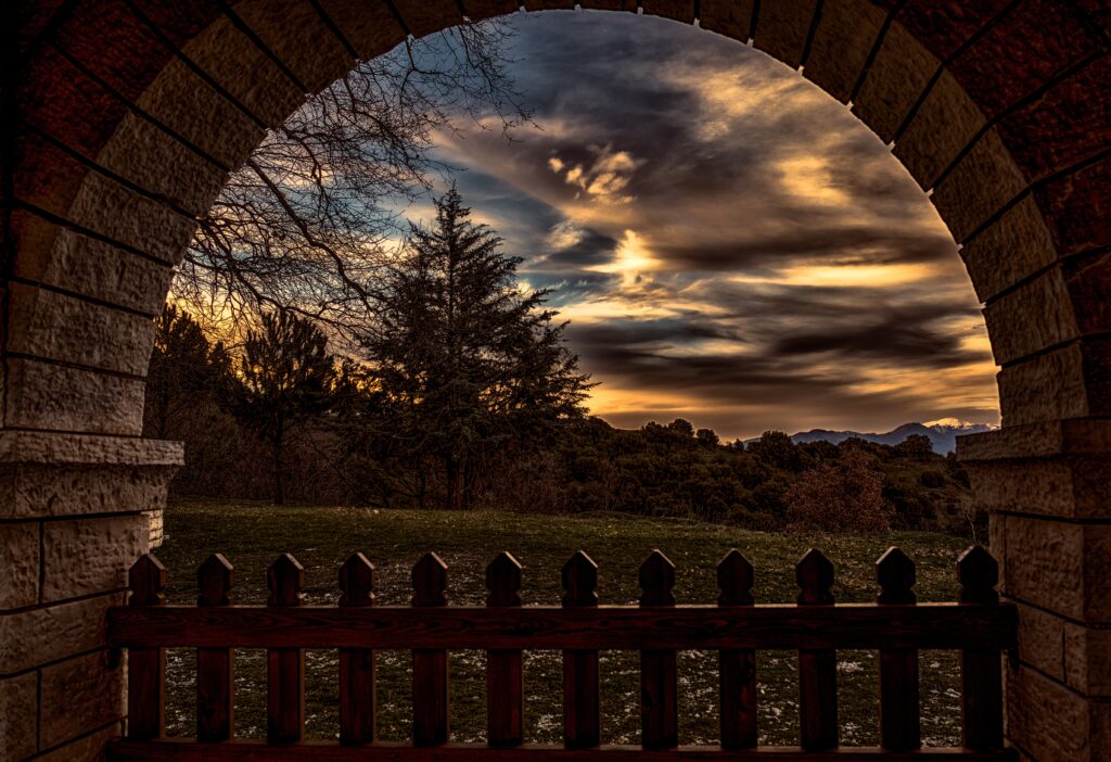 Dramatic sunset with vibrant orange clouds framed by stone arch silhouetted trees rustic fence Wallpaper
