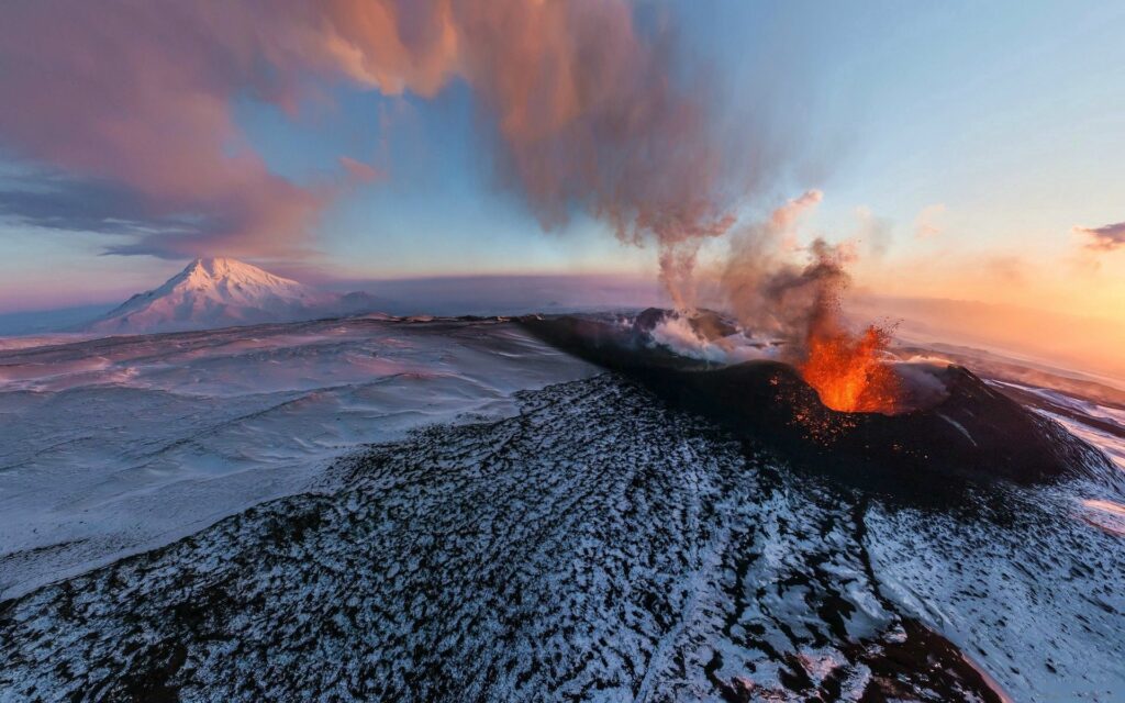 Dramatic sunset volcano eruption with lava over snow-covered mountain landscape wallpaper background