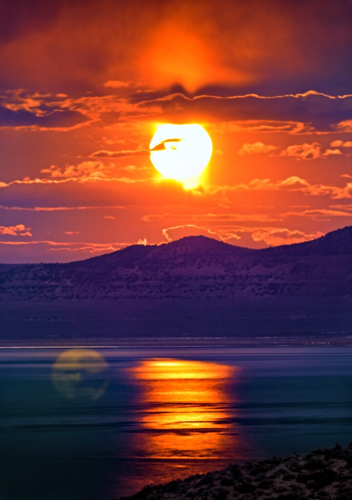 Dramatic sunset wallpaper with glowing sun orange clouds silhouetted mountains golden sea reflection