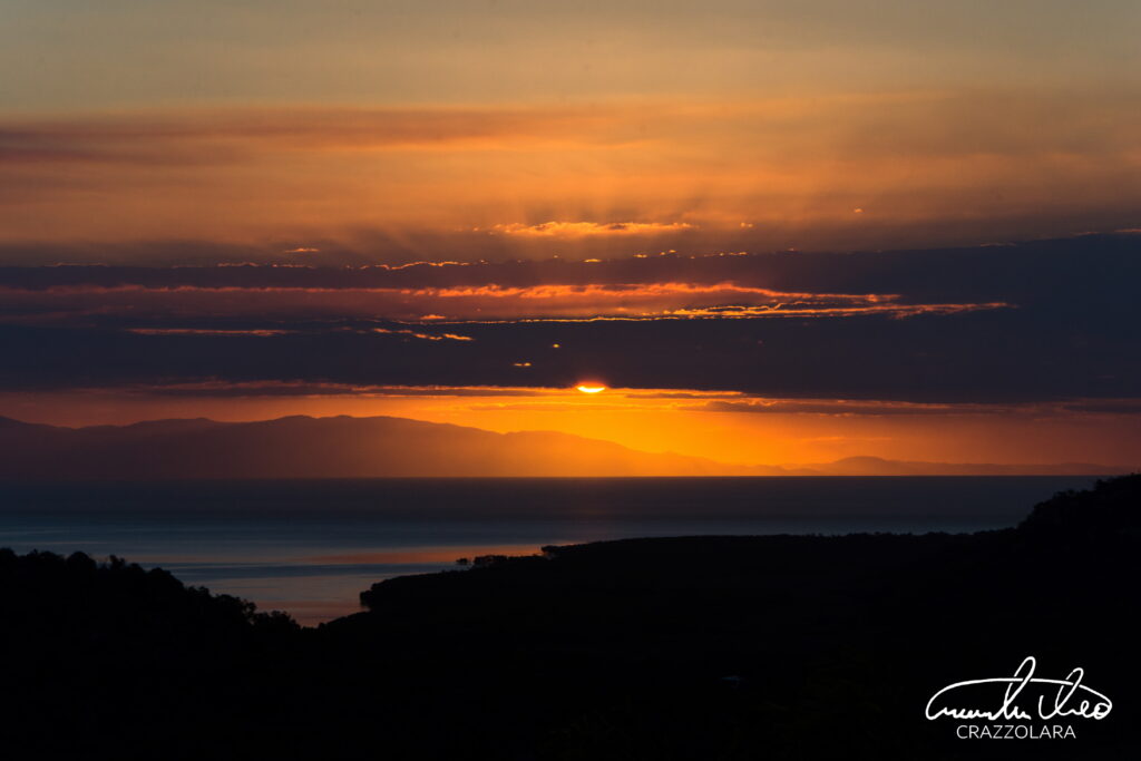 Dramatic sunset wallpaper with vibrant orange gold sky sun behind clouds over calm sea silhouette