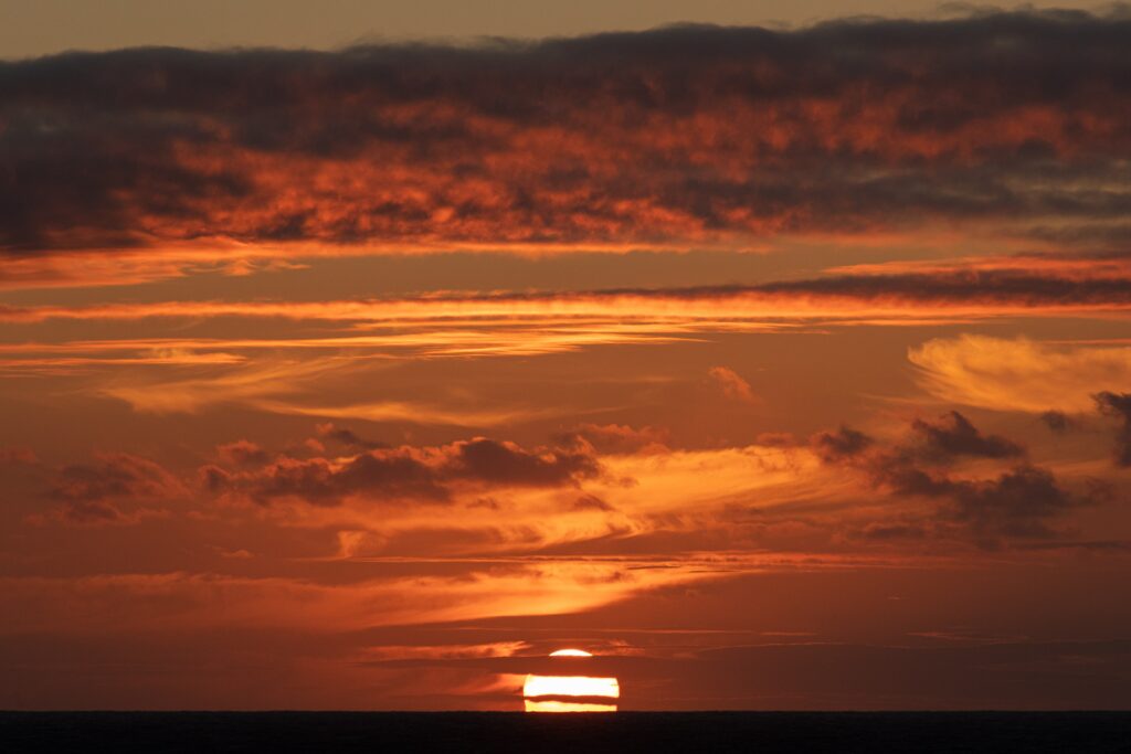 Dramatic sunset wallpaper with vibrant orange red hues and layered clouds over dark horizon