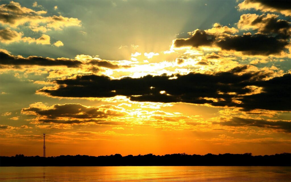 Dramatic sunset wallpaper with orange golden sky clouds reflecting on calm water horizon