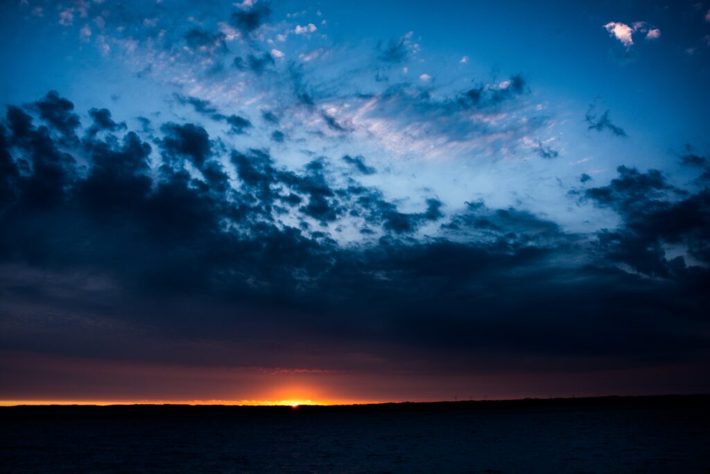 Dramatic sunset wallpaper with glowing orange horizon blue purple sky and dark land reflection