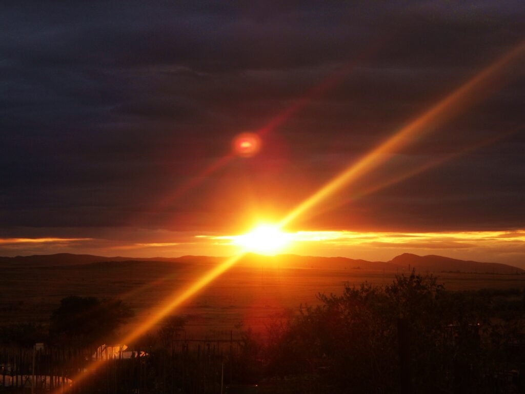 Dramatic sunset with vivid orange sunbeams over open plains and distant mountains wallpaper background