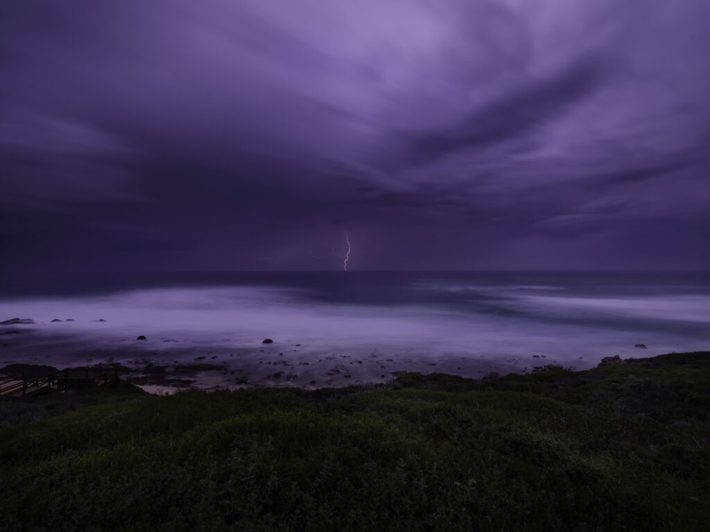 Dramatic coastal thunderstorm wallpaper purple sky lightning over vast sea misty waves greenery