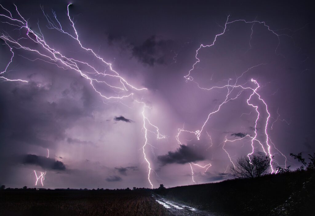 Dramatic thunderstorm with vivid lightning over rural field and winding road at night purple sky Wallpaper