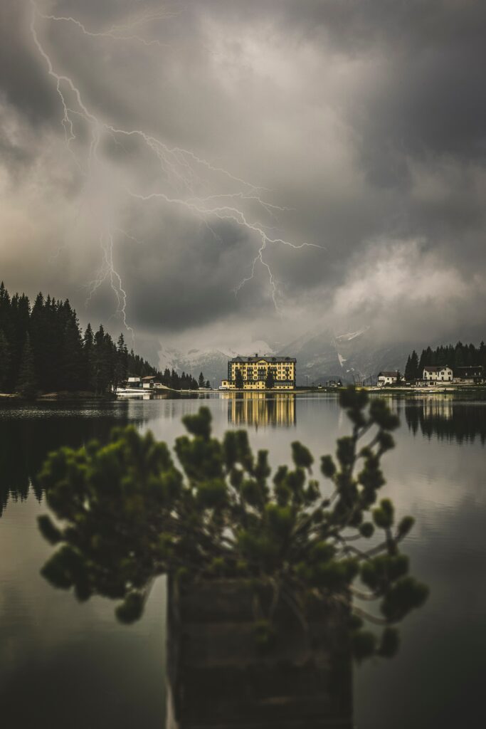 Dramatic thunderstorm over lake with lightning dark clouds mountains golden building reflection Wallpaper