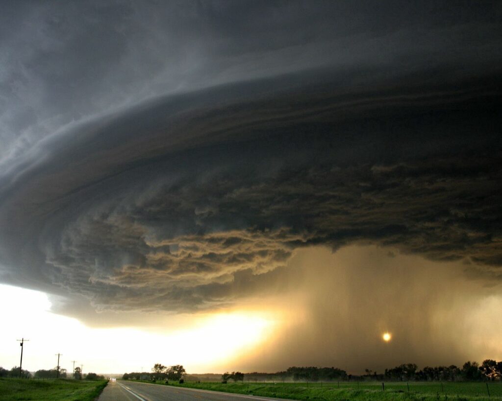 Dramatic tornado funnel over open field and road with dark storm clouds and fading sunlight Wallpaper