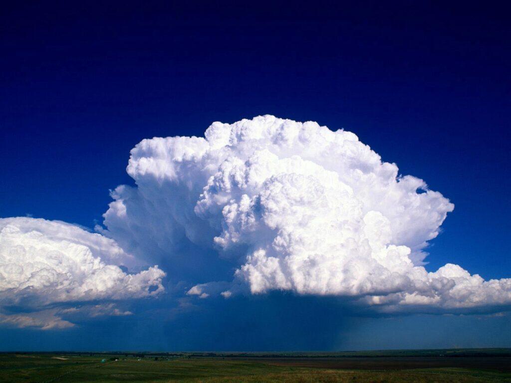 Towering cumulus cloud over open field under deep blue sky stormy dramatic wallpaper background