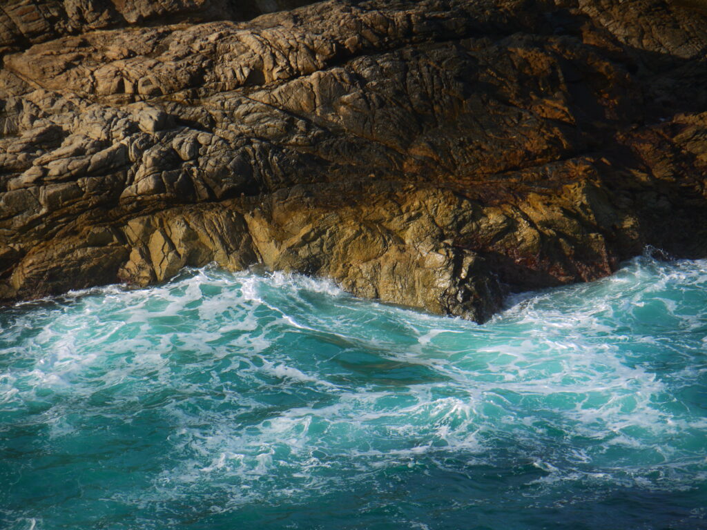 Dramatic coastal wallpaper with turquoise waves crashing foamy surf on rugged weathered rocks