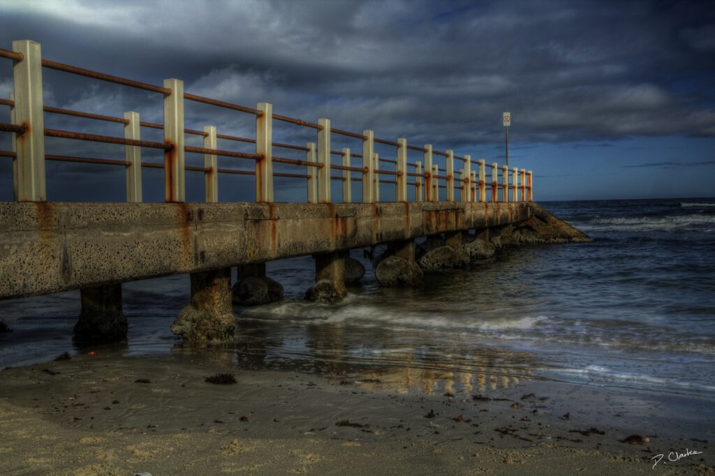 Twilight beach wallpaper with weathered bridge under moody clouds and golden blue hues