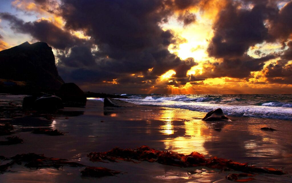 Dramatic twilight coastline with heavy clouds golden sunset wet stones and reflective sand wallpaper